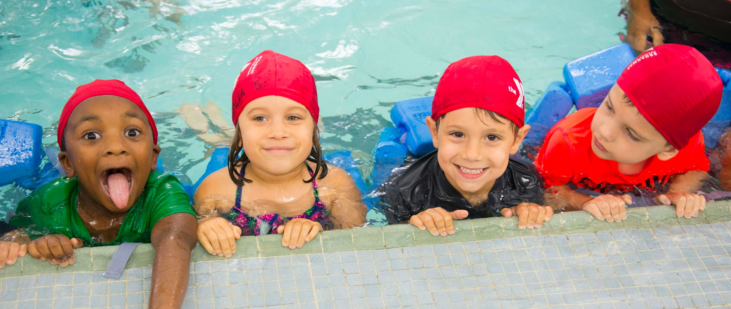 Four summer campers swimming on side of indoor YMCA pool