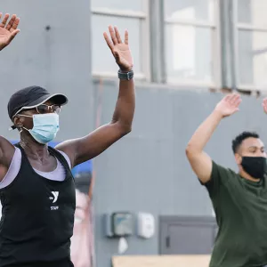 A YMCA instructor and a participant, both in masks, doing jumping jacks in an outdoor fitness class at the Y.