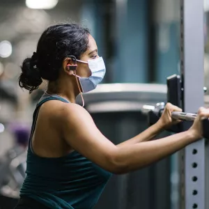 A woman in a mask works out lifting a barbell at the YMCA.