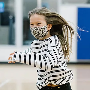A girl in a mask runs and smiles at the YMCA.