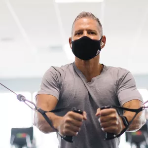 A man in a mask works on strength training at the YMCA.