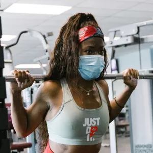 A woman in a mask lifts weights at the YMCA.