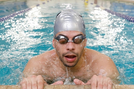 Adult wearing googles takes a breath on the side of North Brooklyn YMCA's indoor lap swimming pool