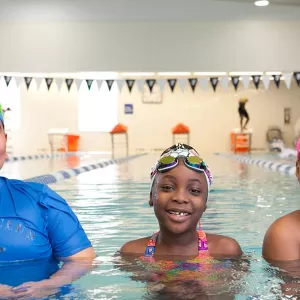 Three kids learning to swim in lap lane of indoor YMCA pool