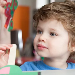 Boy holding popsicle stick craft project at Brooklyn YMCA class for kids