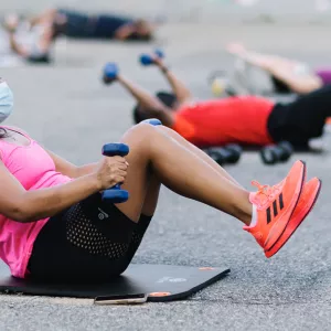 A woman in a mask works out with free weights outdoors at the YMCA.