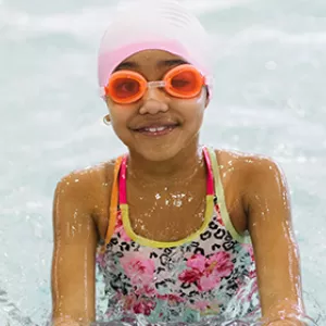 A girl posing for a picture in the pool with goggles and swim cap on